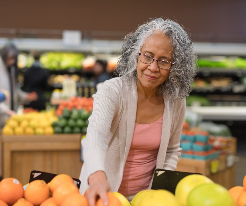 This photo shows a senior woman looking at fruit at the grocery store.