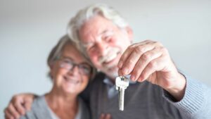 This image represents a couple moving with Medicare. The couple is smiling and the man holds a house key.