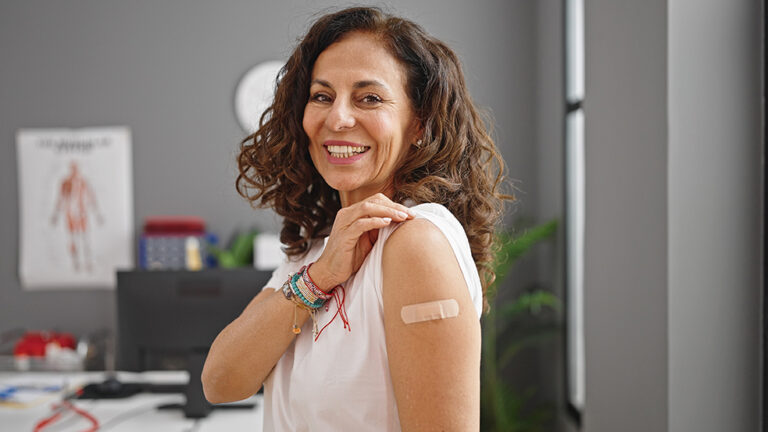 Do I need the measles booster? Middle age hispanic woman smiling confident standing with band aid on arm at clinic