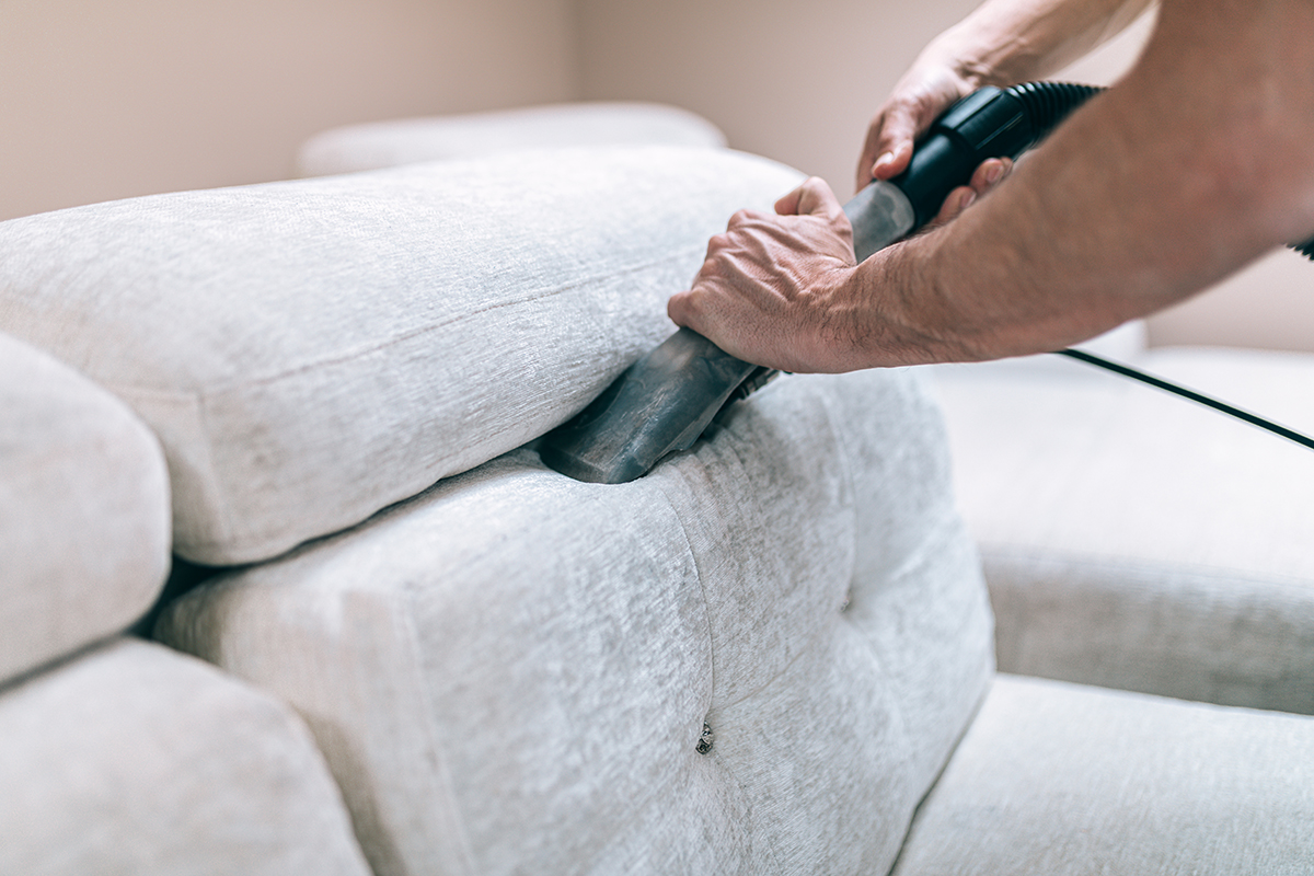 Spring cleaning for seniors. Person deep cleaning sofa with vacuum