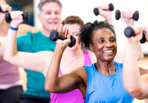 Does Medicare cover weight loss drugs? Close-up of a senior African-American woman in her 60s enjoying an exercise class. She is with a multiracial group of mature adults sitting on fitness balls and lifting hand weights.